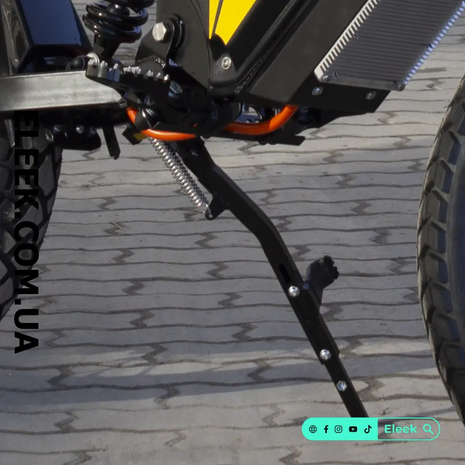 ELEEK At-kick Z415 telescopic kickstand installed on an Atom e-bike, supporting the bike on paving stones